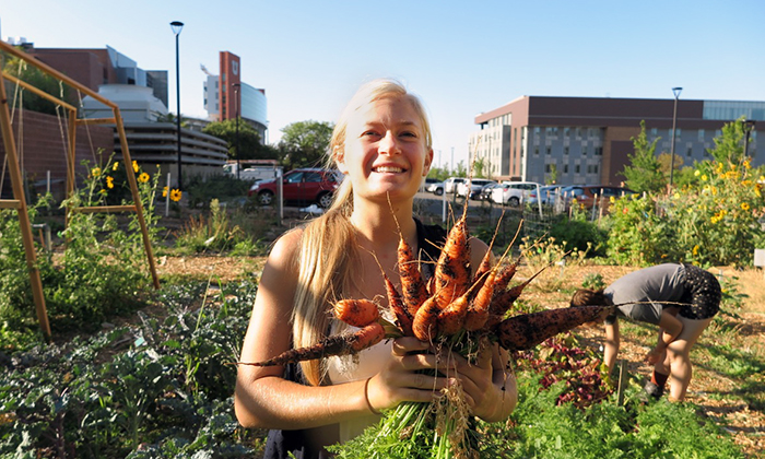An intern with the Sustainability Office's Edible Campus Gardens shows off a carrot harvest.