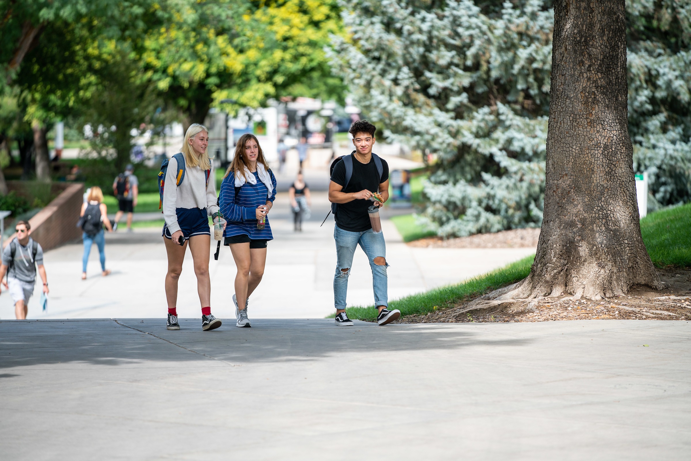 Three students walk on campus between the Union and Marriott Library.