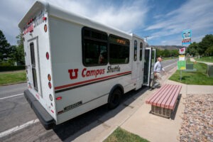 A campus shuttle picks lets off a rider on a sunny, early summer day. Wispy clouds are in the sky.